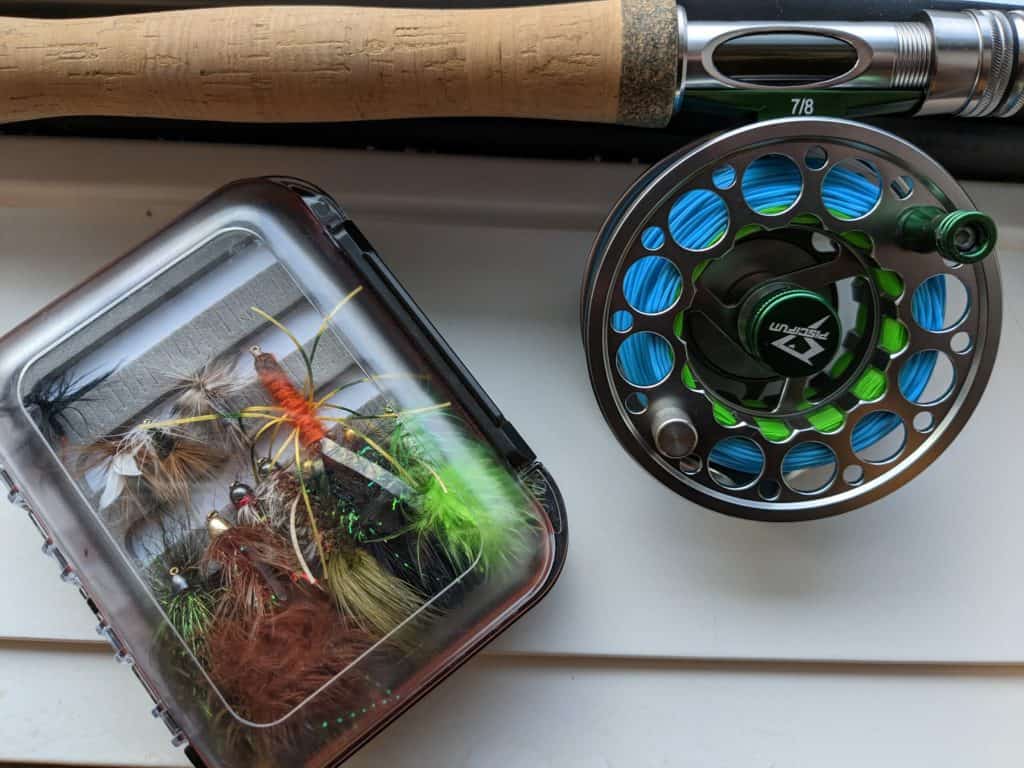 Angler setting up fly fishing gear on a serene lakeshore, ready to embark on a bass fly fishing adventure.