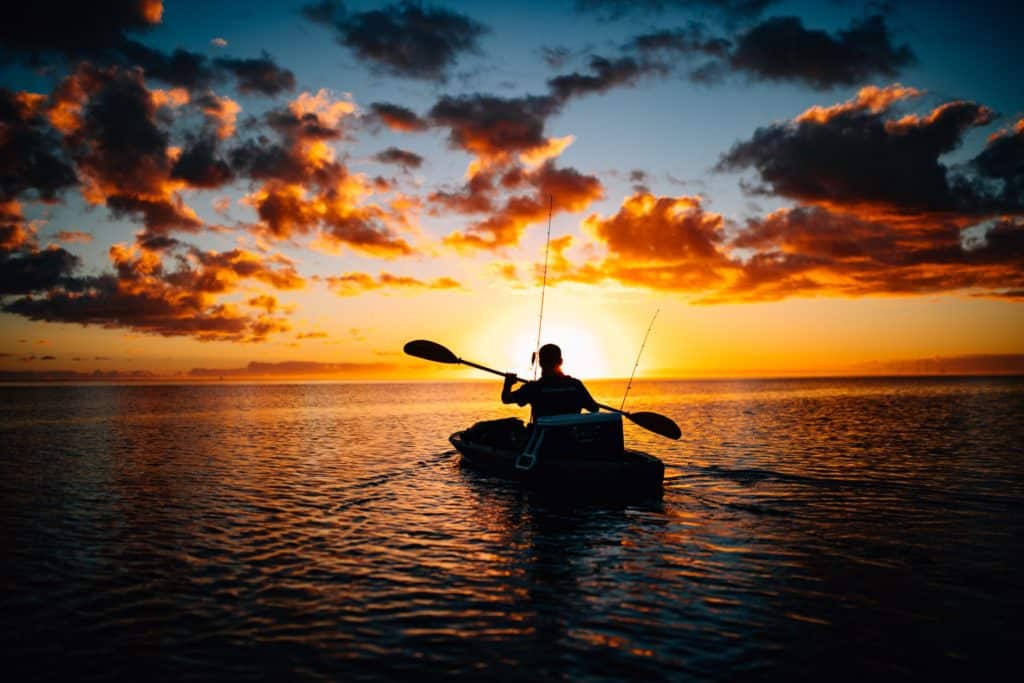 Captivating image of an angler experiencing the tranquility of early morning kayak bass fishing. With the sunrise painting the sky in hues of orange and gold, the serene water sets the stage for a potentially rewarding bass fishing adventure.