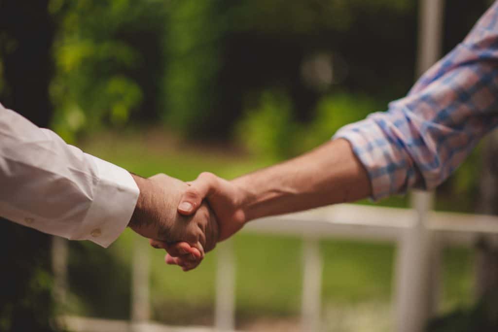 Angler and farmer sealing a fishing agreement with a handshake by a private pond.