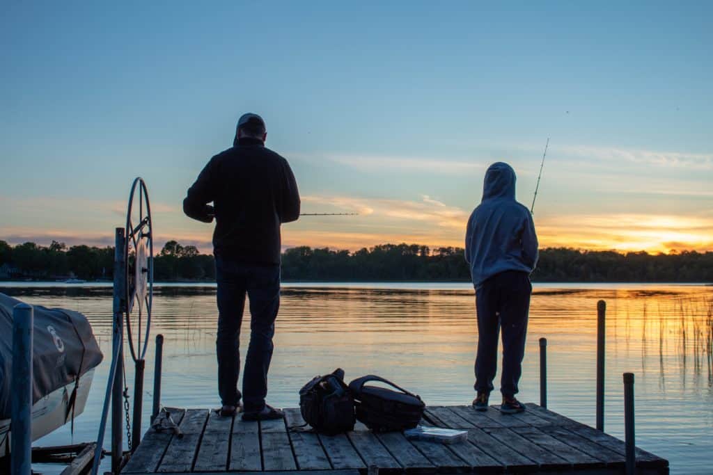 Two anglers casting lines from a wooden dock amidst calm waters.