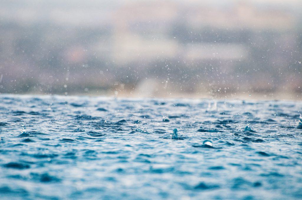 Angler braving heavy rainfall on a lake, casting a line in hopes of a bass bite during a storm.