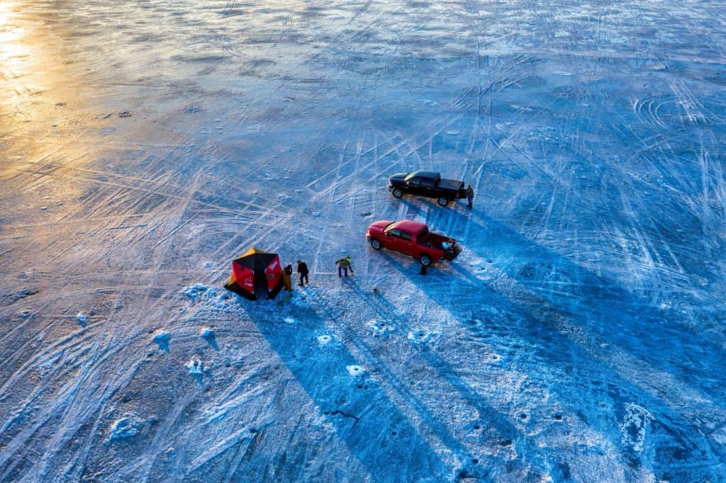 Essential ice fishing gear including auger, tackle, rods, bait, and insulated boots laid out on snowy surface